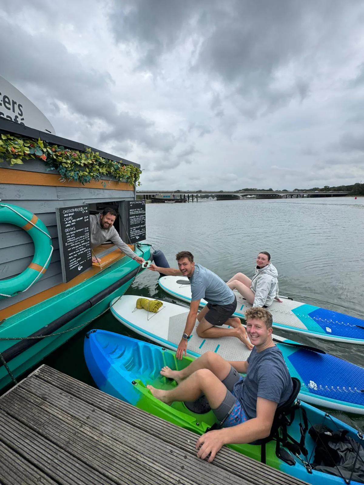 Paddlers on kayaks and paddleboards being served at the floating cafe on the River Hamble