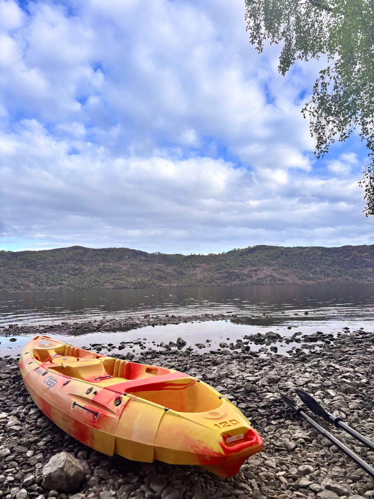 A Yak Shack kayak resting on the rocky shore of Loch Ness with the Highland hills beyond