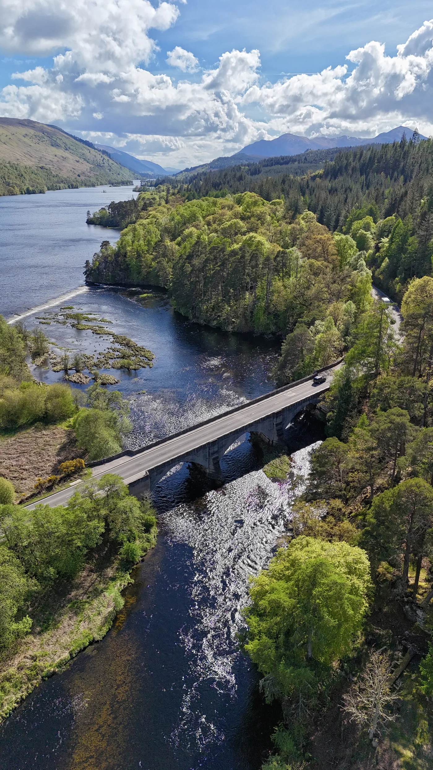 Aerial view of the bridge over the River Oich flowing out of Loch Oich, surrounded by forest and Highland hills