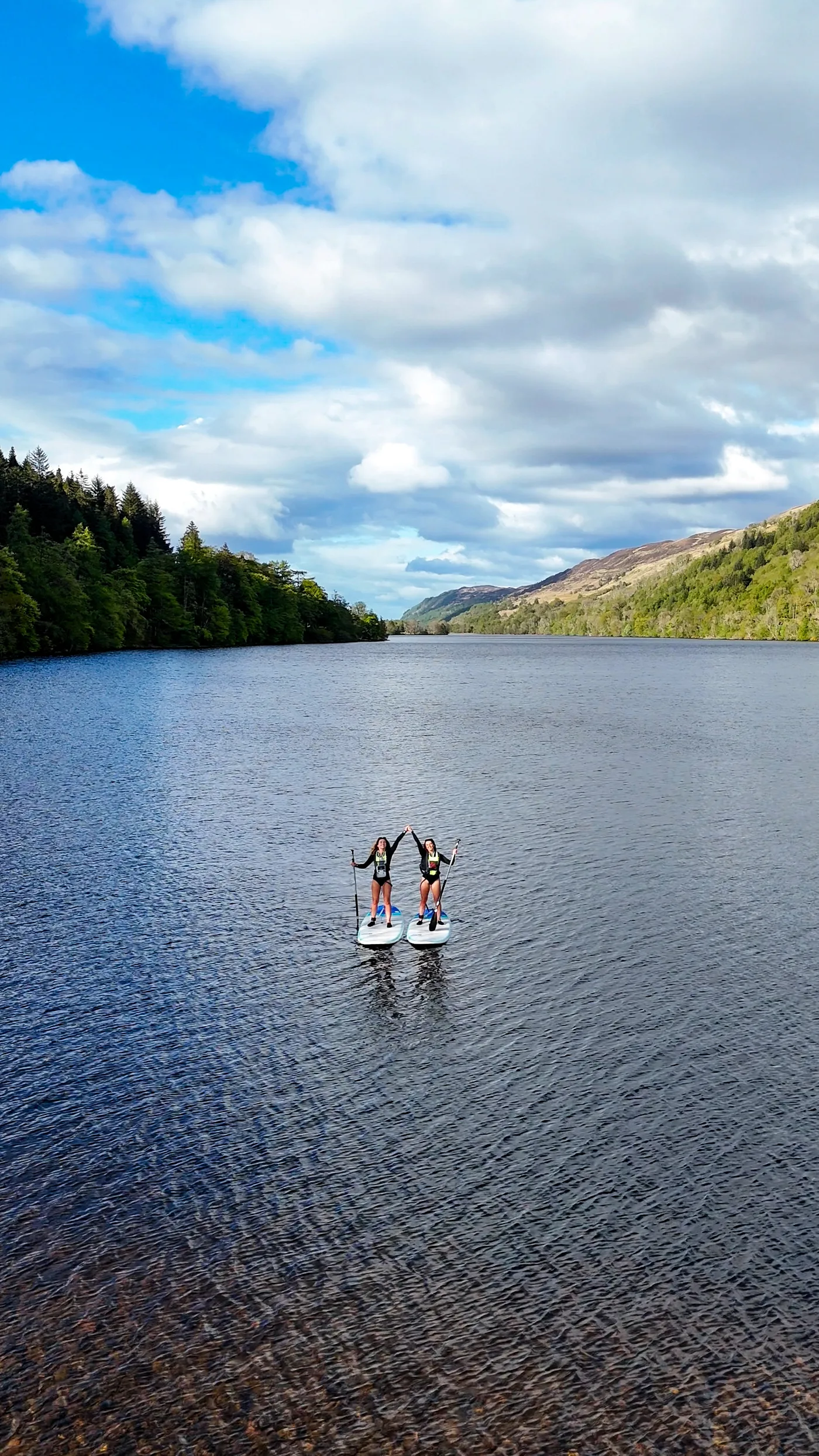 Two paddleboarders on Loch Oich seen from above, surrounded by Highland hills and forest in the Great Glen